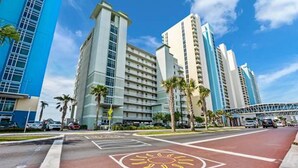 A multi-story hotel with a modern design, featuring a prominent sun symbol on the pavement, palm trees, and a clear blue sky. - Relax in Rare Low-Density Luxury – Marisol 3BR Beachfront Condo (Panama City Beach)