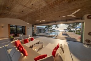 Un interior moderno con vista a la piscina, techo de madera y mobiliario blanco.