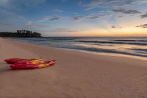 Una playa con kayaks y un mar tranquilo al atardecer.