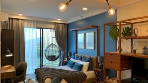 A bedroom with a bed, desk, chair, hanging chair, and a large window. - Deluxe Holiday Studio Suite @ Timurbay w/ Seaview (Kuantan)