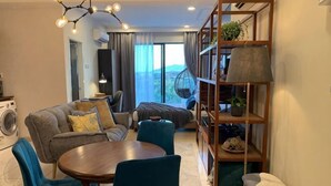A modern living room with a sofa, chairs, a round table, and a bookshelf. - Deluxe Holiday Studio Suite @ Timurbay w/ Seaview (Kuantan)