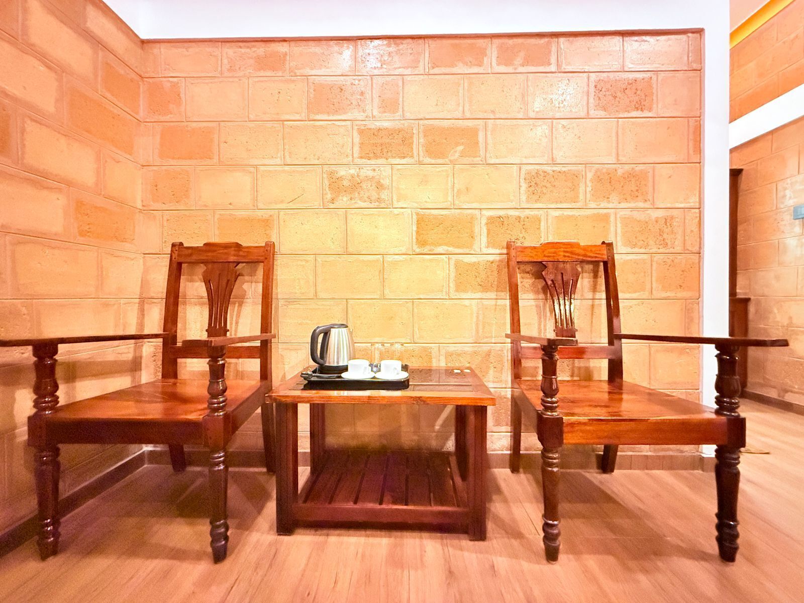 A corner room with two wooden chairs, a small table, and a kettle.
