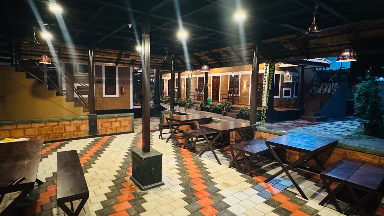 An outdoor dining area with wooden tables and benches, surrounded by brick walls and potted plants.
