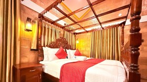 A bedroom with a wooden four-poster bed, a nightstand, and a wall-mounted lamp. - CREDIBLE HERITAGE RESORT (Varkala)