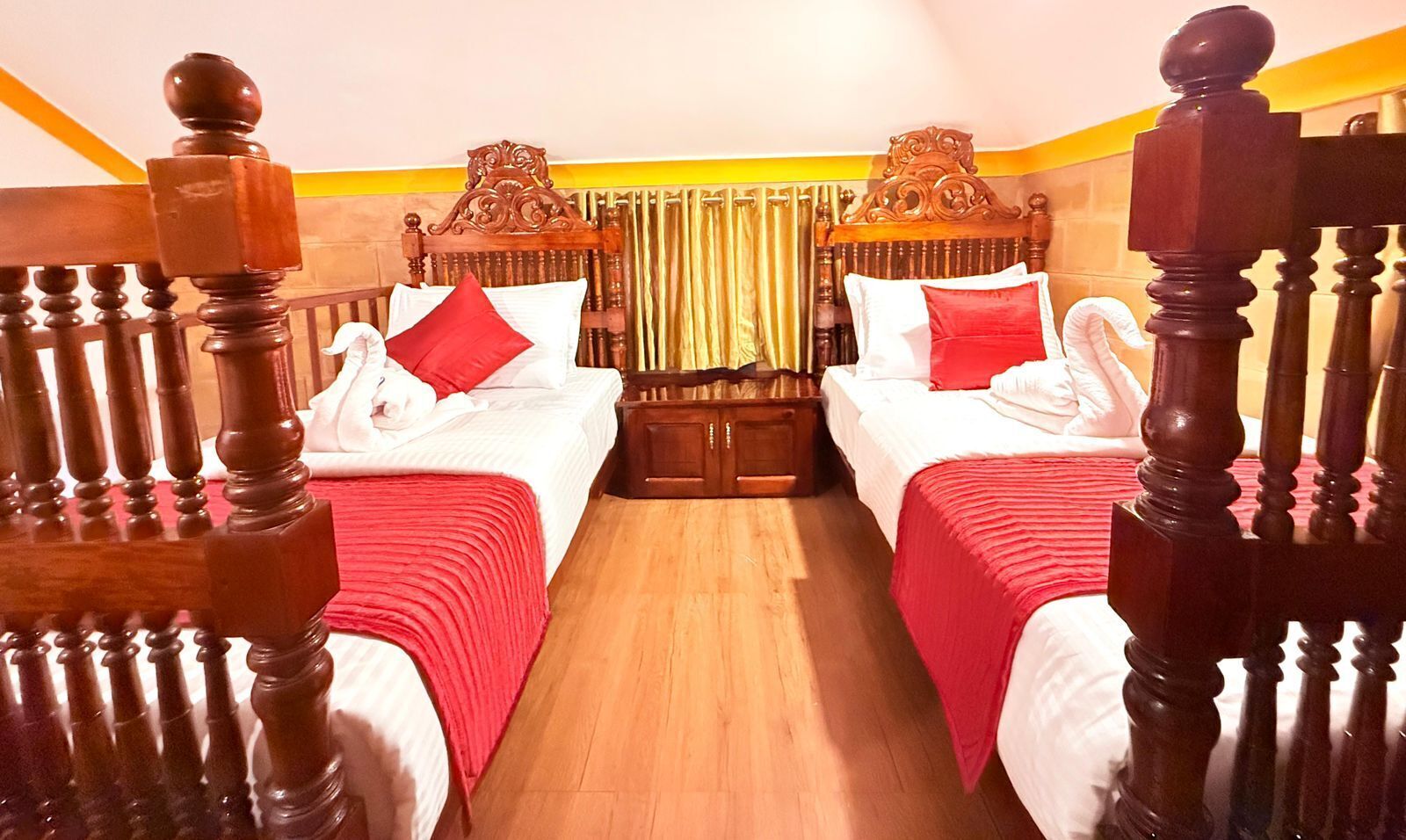 Habitación de hotel con dos camas, cada una con cabecero de madera y ropa de cama roja.