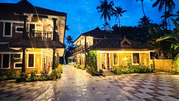 A traditional building with a tiled entrance and a balcony, surrounded by lush greenery and palm trees. - CREDIBLE HERITAGE RESORT (Varkala)