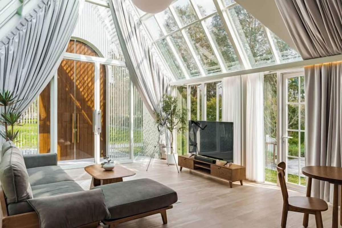 Un salon moderne doté d’un grand plafond en verre, d’un canapé, d’un téléviseur et de meubles en bois.