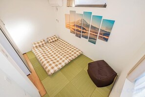Ein kleines Zimmer mit einem Bett, einer grünen Matte, einem braunen Sitzsack und drei an der Wand hängenden Bildern.