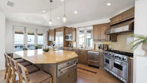 Une cuisine moderne dotée d’un grand îlot central, d’appareils électroménagers en acier inoxydable et de meubles de rangement en bois.