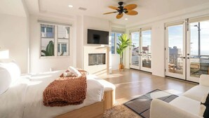 Une chambre spacieuse avec un grand lit, un ventilateur de plafond, une télévision et une porte-fenêtre coulissante donnant sur un balcon.