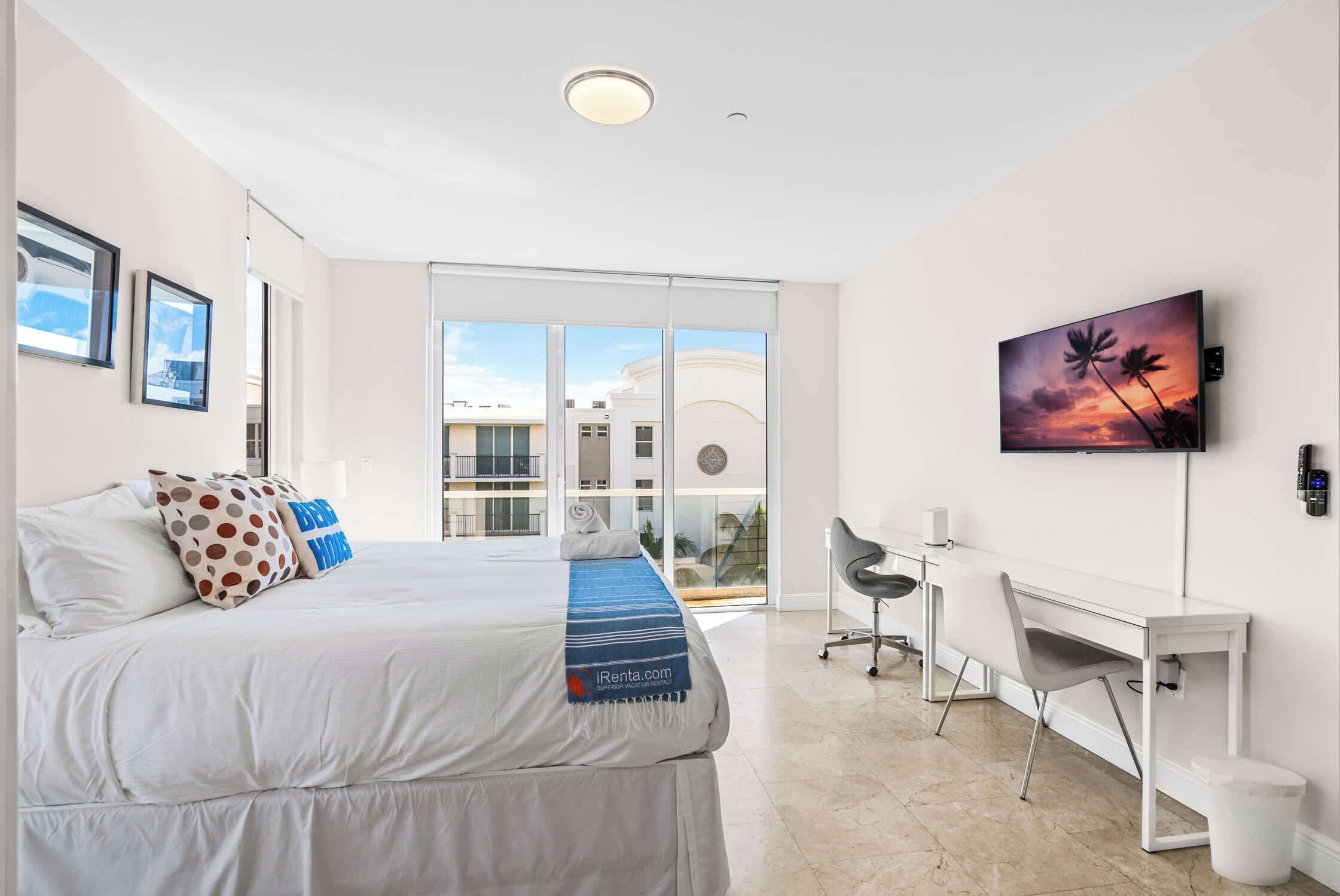 A modern hotel room with a bed, a desk, and a large window.