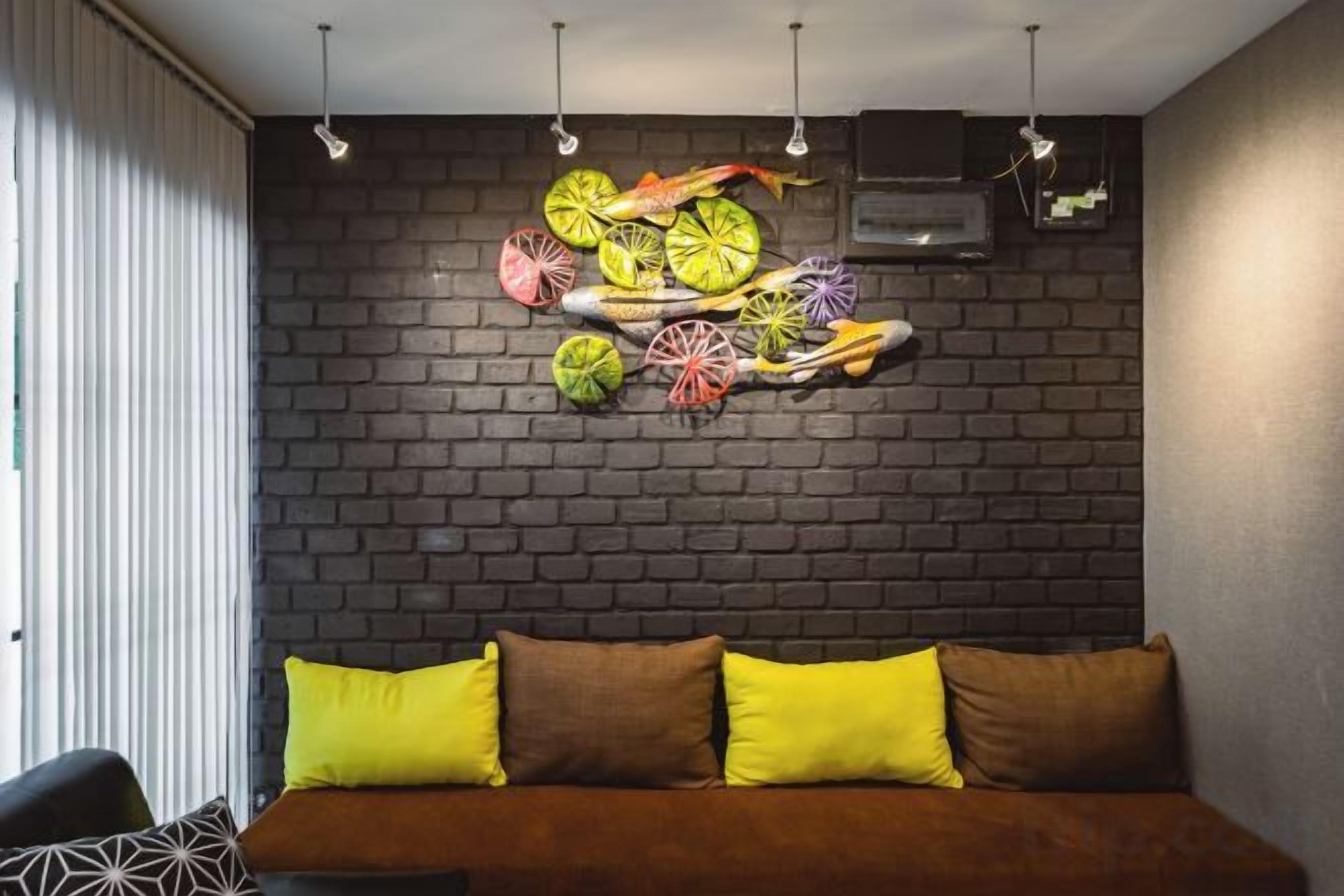 A room with a brick wall, a brown sofa with yellow cushions, and a decorative wall art piece.