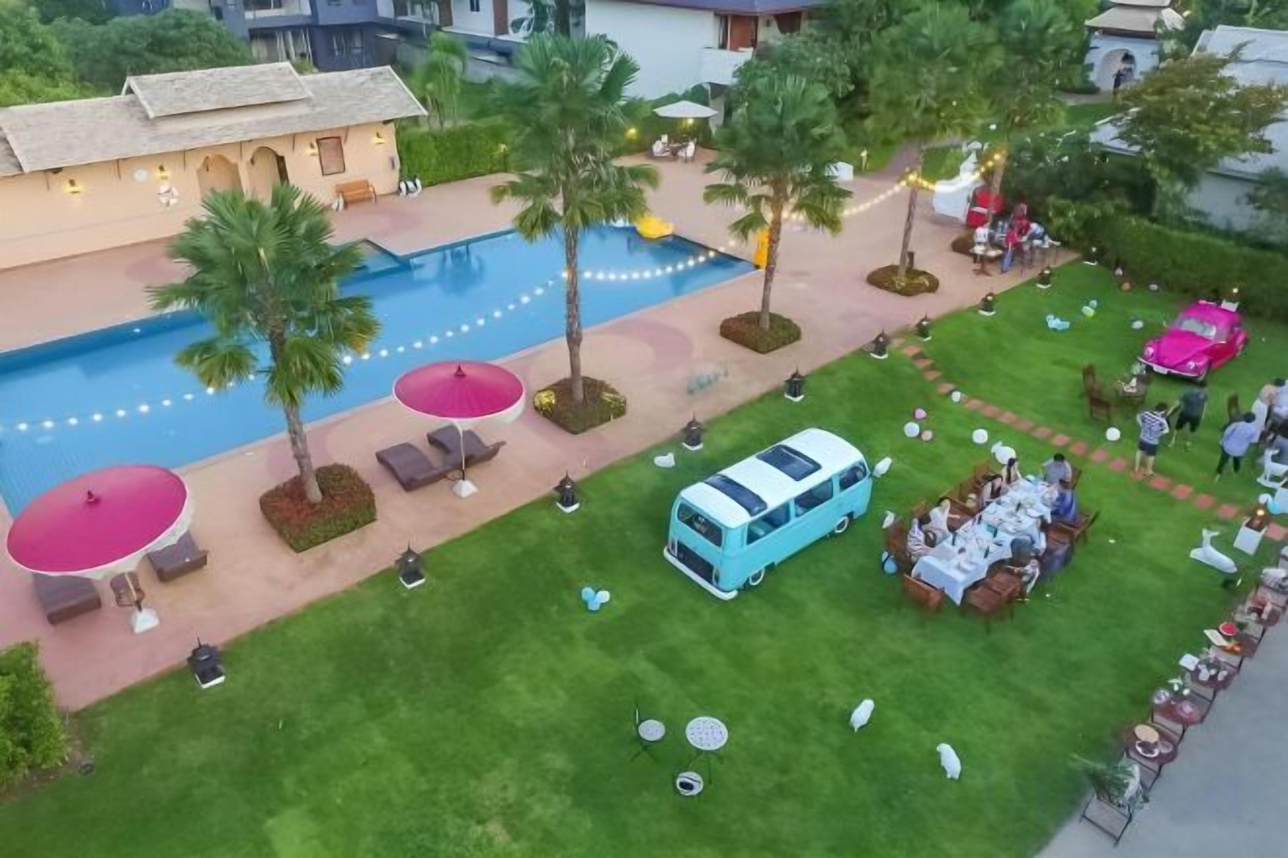 Un área de piscina con sillones reclinables, una camioneta azul y una zona de comedor con mesas y sombrillas.
