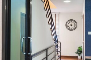 A staircase with a metal railing leading to a landing, a wall clock, and a potted plant. - Baan PromTel , Luxury Villa close to Nimman, Resort Pool, 4BR (Chiang Mai)
