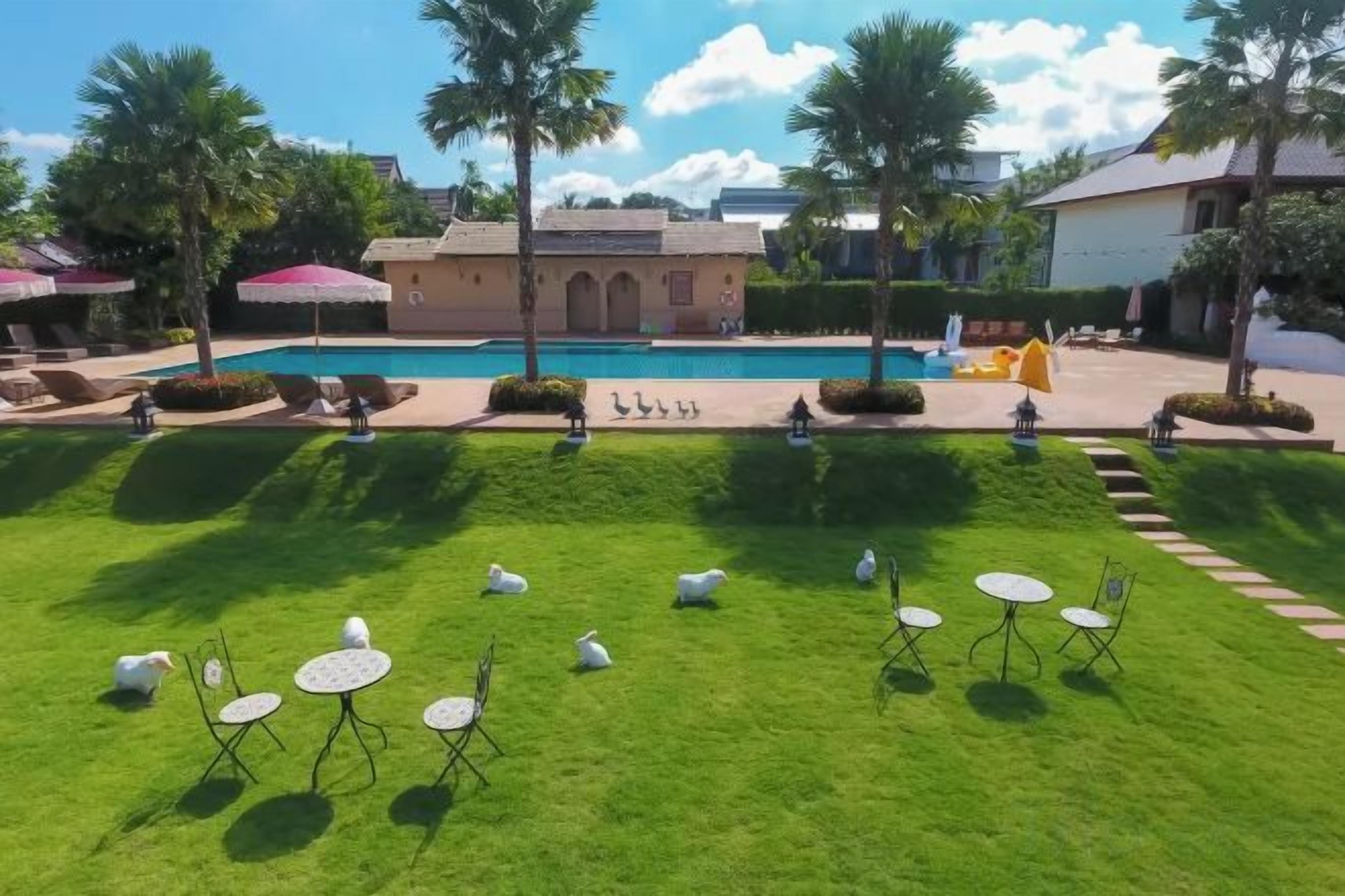 Un área de piscina con césped, sillas de descanso y sombrillas.