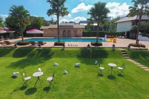 A pool area with a grassy lawn, lounge chairs, and umbrellas. - Baan PromTel , Luxury Villa close to Nimman, Resort Pool, 4BR (Chiang Mai)