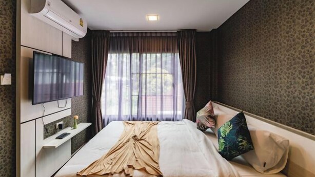 A hotel room with a bed, a flat-screen TV, an air conditioning unit, and a window with curtains. - Baan PromTel , Luxury Villa close to Nimman, Resort Pool, 4BR (Chiang Mai)
