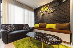 A modern living room with a black sofa, a glass coffee table, and a brick accent wall. - Baan PromTel , Luxury Villa close to Nimman, Resort Pool, 4BR (Chiang Mai)