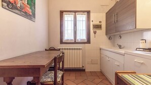 A compact kitchen with a wooden table, a radiator, and a window with curtains. - 3T Tripla  Affitti Brevi Italia  · 3T Tripla - Affitti Brevi Italia (Modena)