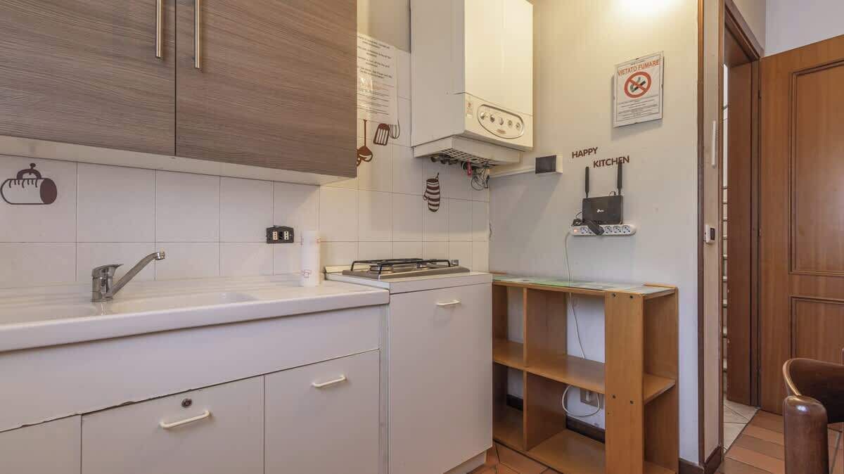 Et moderne køkken med hvide skabe, en stålvask og en indbygget komfur. Der er en hylde i træ og et skilt med teksten "HAPPY KITCHEN".
