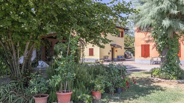 A courtyard with potted plants, a covered seating area, and a building with red shutters. - 3T Tripla  Affitti Brevi Italia  · 3T Tripla - Affitti Brevi Italia (Modena)