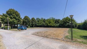 A parking area with a blue car, a gravel path, and a grassy field. - 3T Tripla  Affitti Brevi Italia  · 3T Tripla - Affitti Brevi Italia (Modena)