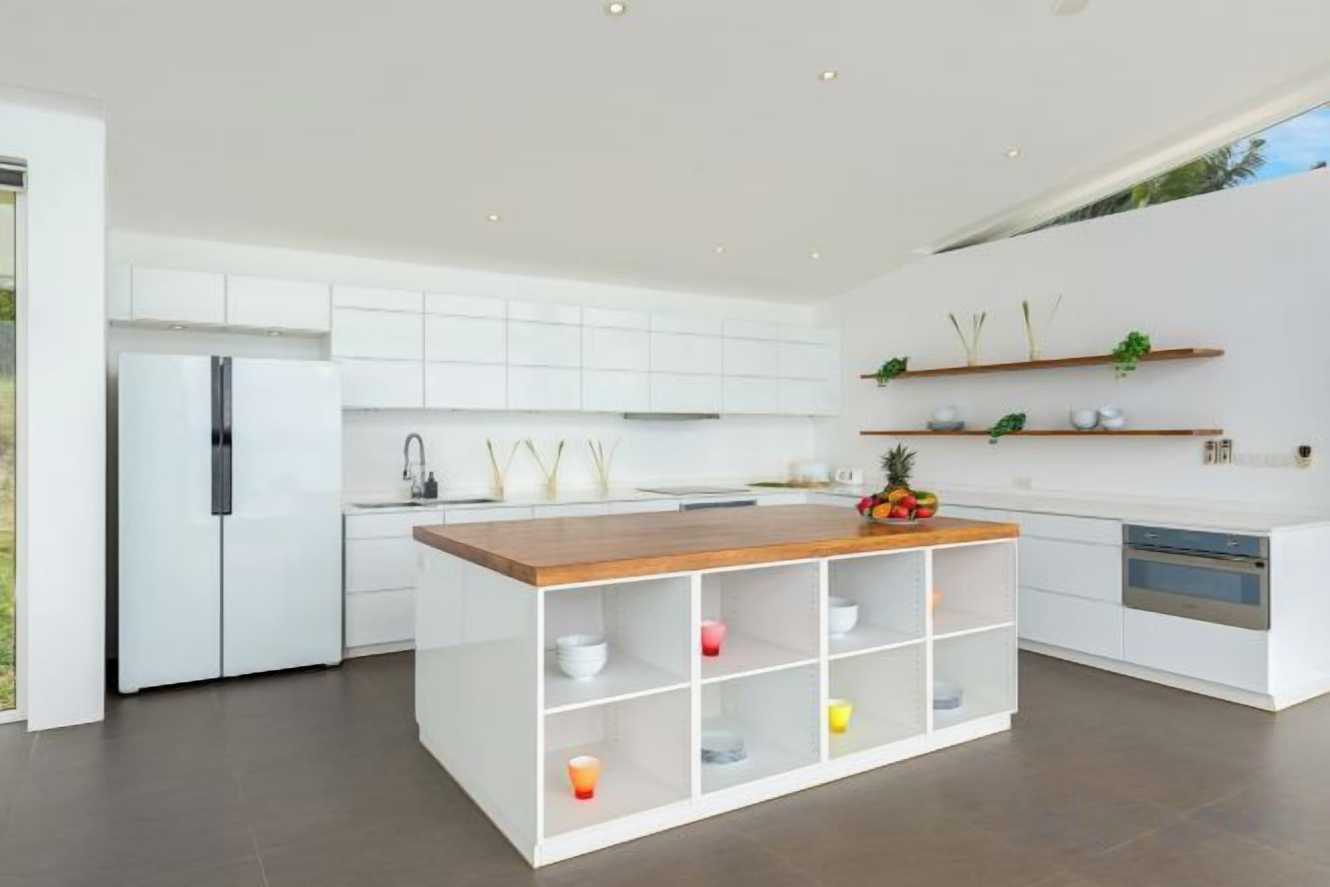 A modern kitchen with white cabinetry, a wooden island, and built-in appliances.