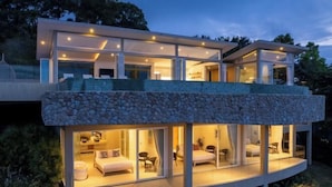 A modern two-story house with a stone facade, large glass windows, and a balcony. - Villa Cabo: Hilltop Retreat with Panoramic Ocean Views (Koh Samui)