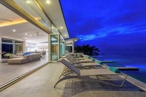 A modern outdoor living area with a pool, lounge chairs, and a view of the ocean at dusk. - Villa Cabo: Hilltop Retreat with Panoramic Ocean Views (Koh Samui)