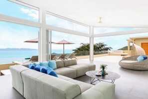 Una sala de estar moderna con un ventanal grande, un sofá, una mesita redonda y un sillón de mimbre.
