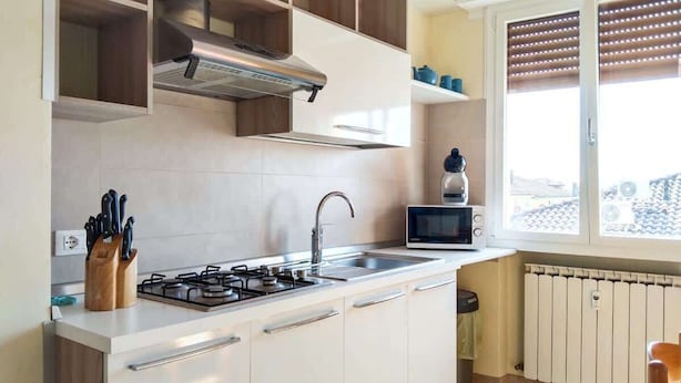 Een moderne keuken met witte kasten, een gasfornuis, een magnetron en een raam met zonwering.