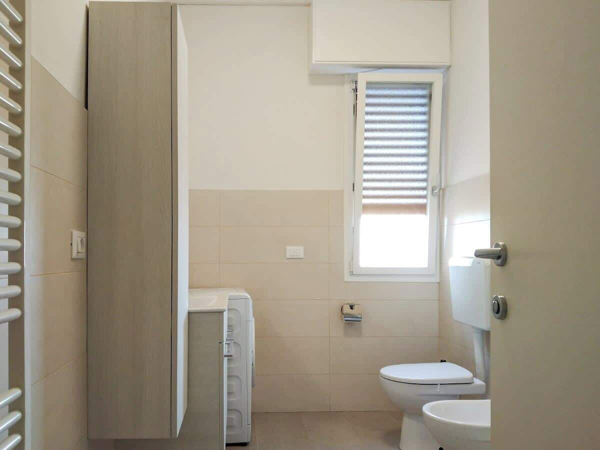Uma casa de banho pequena e limpa, com sanita, janela com persianas e um porta-toalhas.