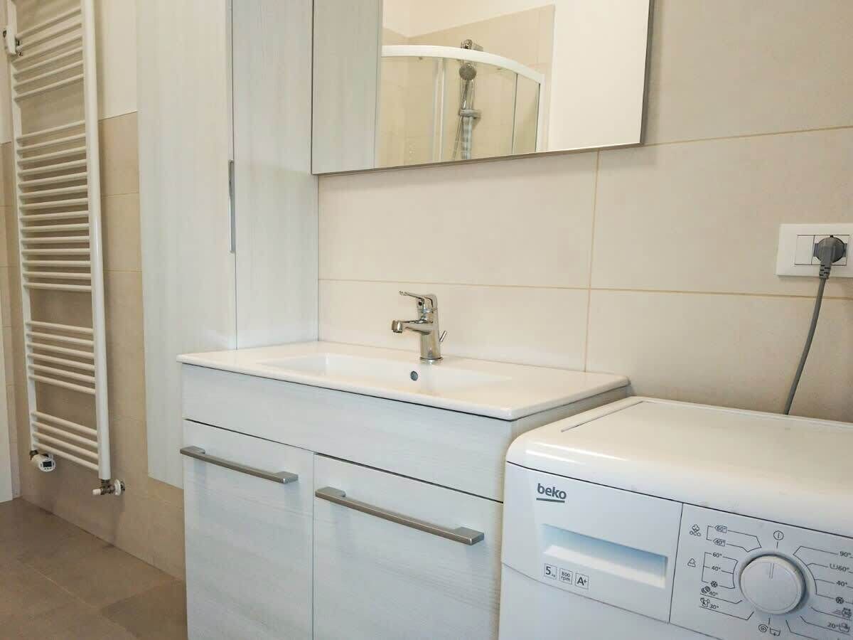Une salle de bain avec un lavabo blanc, un miroir au-dessus, un porte-serviettes et un lave-linge.