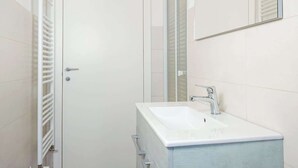 Een badkamer met een witte deur, een witte wastafel met een chromen kraan, en een spiegel boven de wastafel.