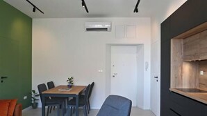 A modern dining area with a table and chairs, a sofa, an air conditioning unit, and a kitchen area with a wooden countertop. - Steps from Palace & Riva - Old Town Pine (Split)