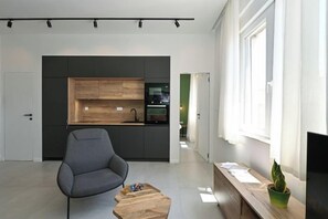 A modern kitchen with dark cabinetry, a wooden countertop, and a built-in oven. There is a gray armchair and a wooden coffee table in the living area. - Steps from Palace & Riva - Old Town Pine (Split)