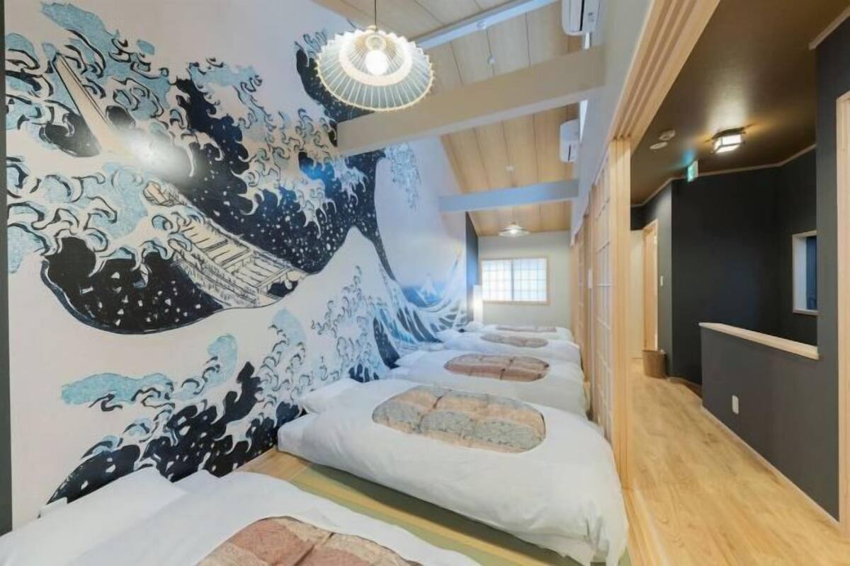 A hotel room with a traditional Japanese wave painting on the wall, a wooden floor, and a bed with white bedding.