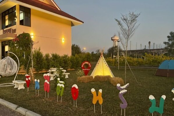 A building with a yellow facade and a red roof, surrounded by outdoor seating and a tent. - New Blessing Home (Nan)