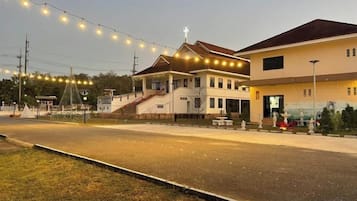 A building with a staircase leading to a second floor, a covered outdoor area, and a street with a fence in the foreground.