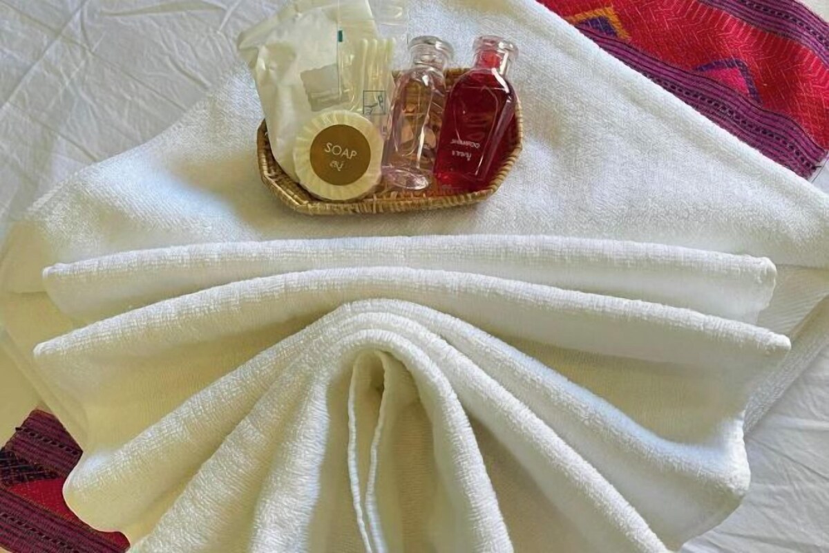 A neatly folded white towel with a tray of toiletries including soap, shampoo, and a bottle of perfume.