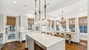 A modern kitchen with a large island, wooden flooring, white cabinetry, and pendant lighting. - Directly NEXT TO Camp WaterColor! 6-Seater LSV/Golf Cart & 4 Bikes Included! (Santa Rosa Beach)