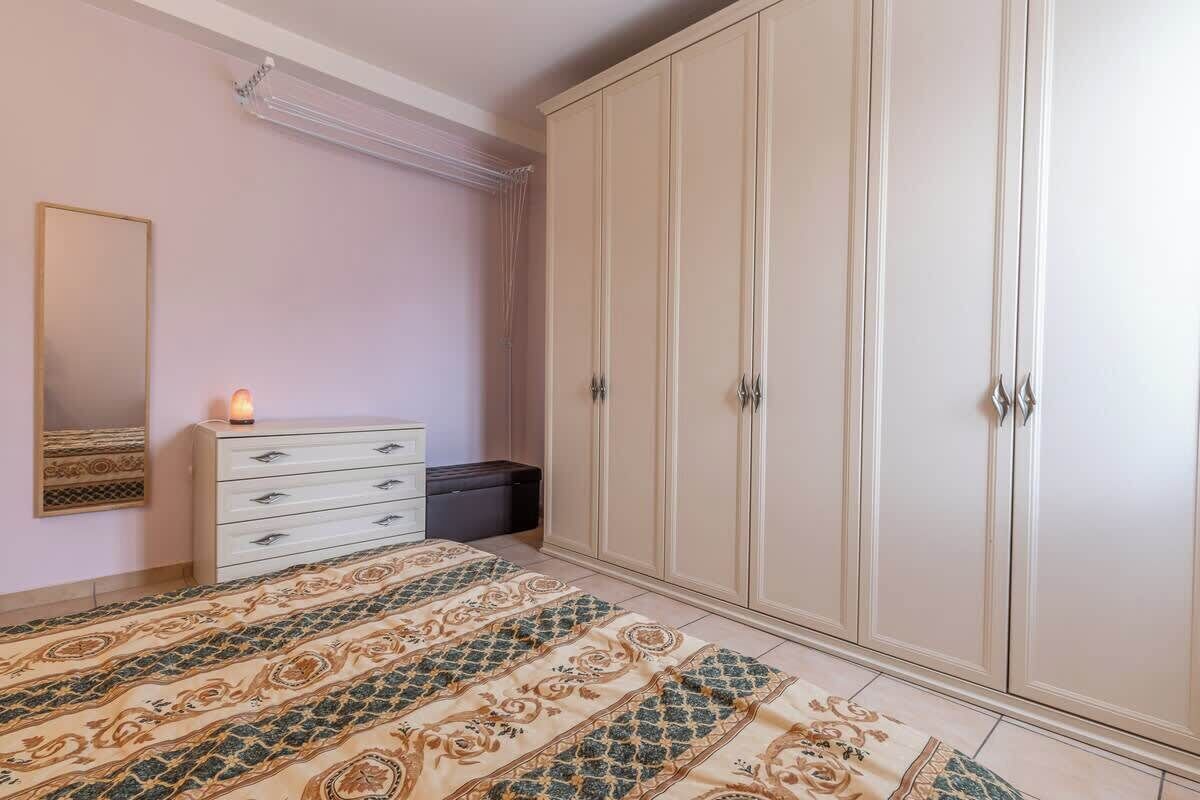 A bedroom with a large wardrobe, a bedside table with a lamp, and a patterned rug.