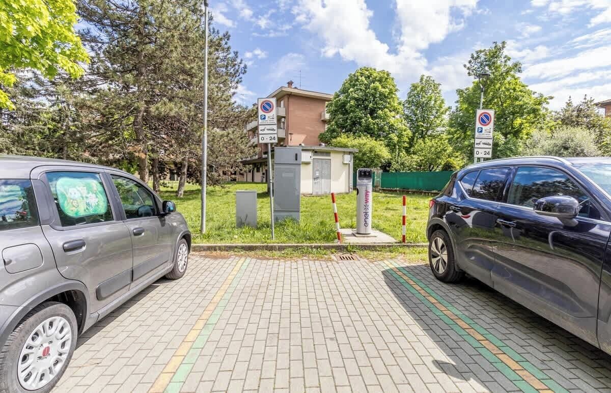 Un espace de stationnement avec deux voitures, un bâtiment en arrière-plan et une clôture verte.