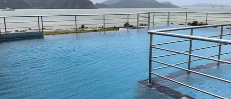 A swimming pool with a metal railing, surrounded by a fence, and a view of distant mountains.