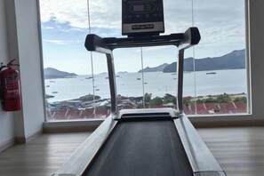 Un cinturó d'entrenament amb pantalla digital, ubicat en una habitació amb un gran finestral amb vista a un cos d'aigua i terres llunyanes.