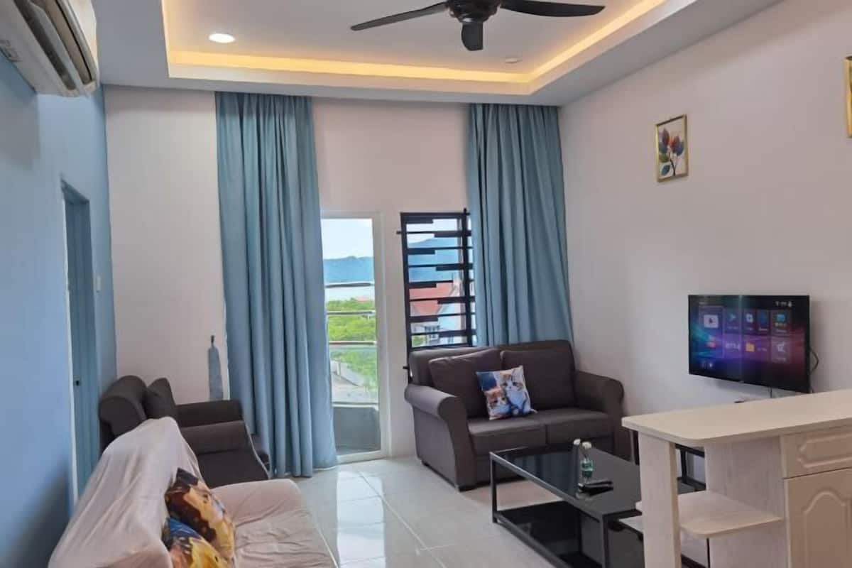 Un salon moderne avec un canapé, une table basse, un téléviseur et un balcon agrémenté de rideaux.