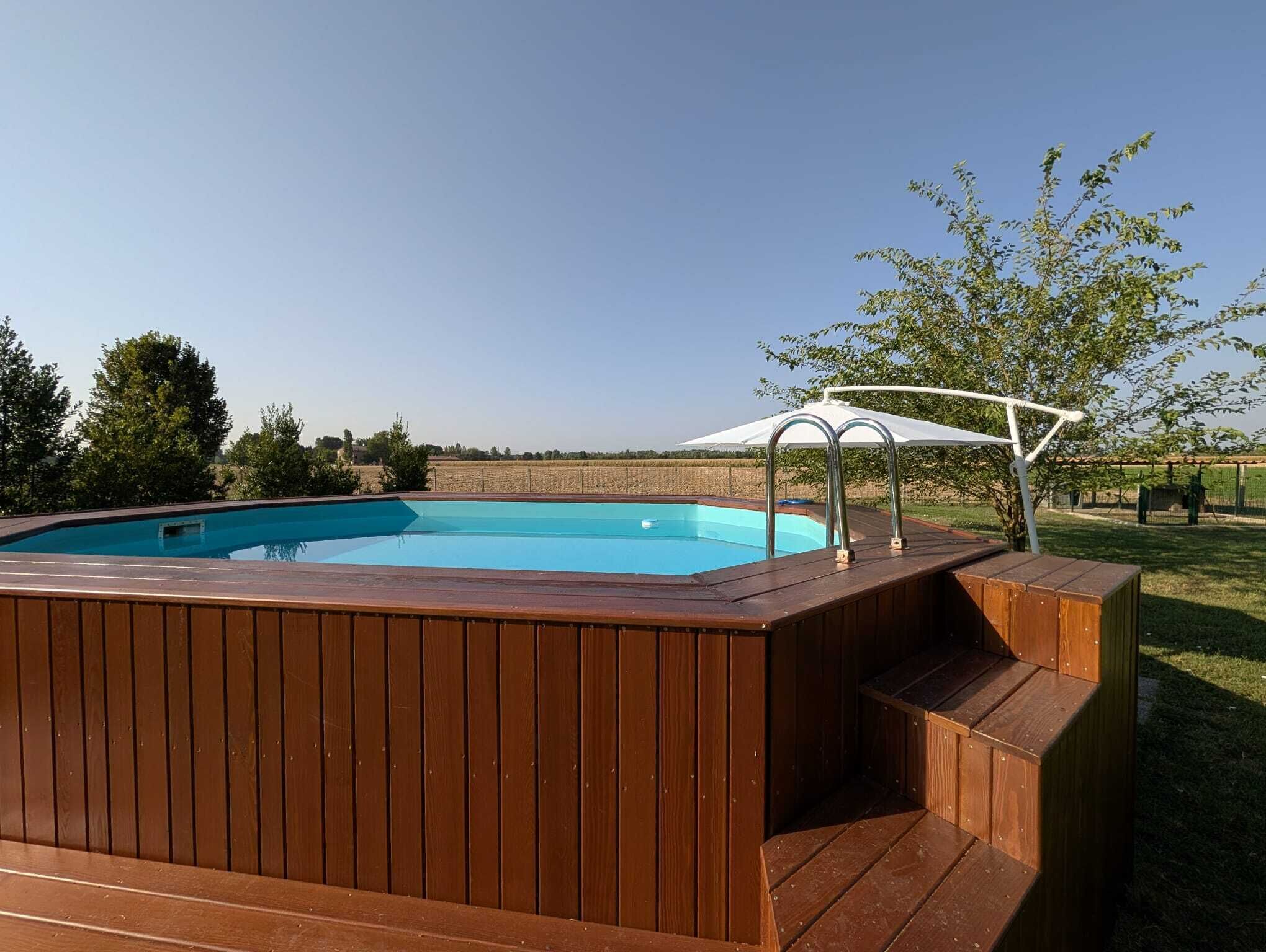 A swimming pool with a wooden deck and a white canopy.