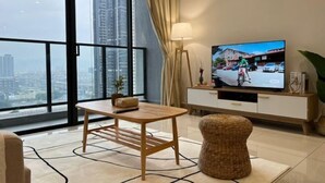 A modern living room with a large window, a television, a table, and a wicker ottoman. - KLCity & KLCC View Modern Style 2R2B - 6 pax (Kuala Lumpur)