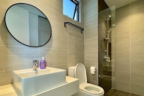 A modern bathroom with a round mirror, a white sink, a toilet, and a glass-enclosed shower. - KLCity & KLCC View Modern Style 2R2B - 6 pax (Kuala Lumpur)