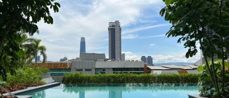 A swimming pool with a view of a city skyline, surrounded by greenery.